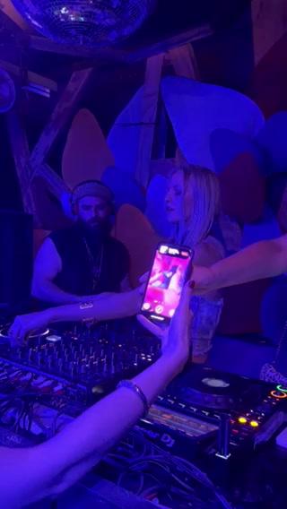 A DJ works at a club while a woman records him on her phone